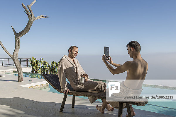 Zwei junge Männer am Pool beim Fotografieren mit digitalem Tablett