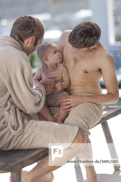 Schwules Paar mit Baby auf Holzbank sitzend