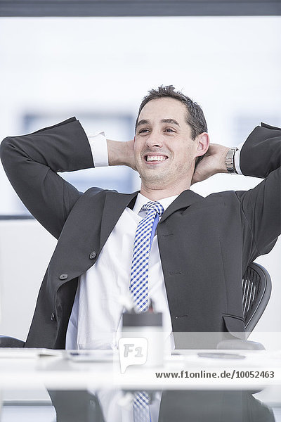 Lächelnder Geschäftsmann im Büro sitzend  Hände hinter dem Kopf