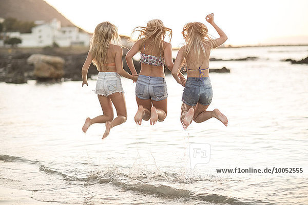 Three young women jumping on a beach in waves