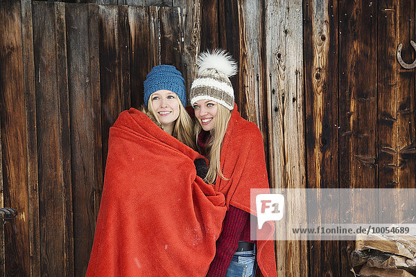 Zwei junge Freundinnen in rote Decke gehüllt außerhalb der Holzhütte