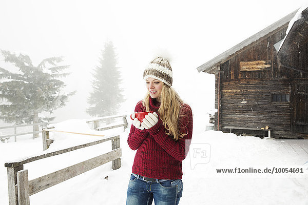 Junge Frau trinkt Kaffee im Schnee außerhalb der Kabine