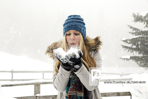 Junge Frau  die eine Handvoll Schnee bläst.