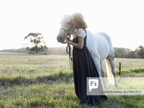 Porträt eines jungen Mädchens mit grauem Pferd im sonnigen Feld