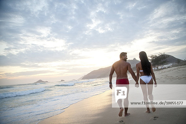 Mid adult couple walking along beach  hand in hand  wearing swimwear  rear view