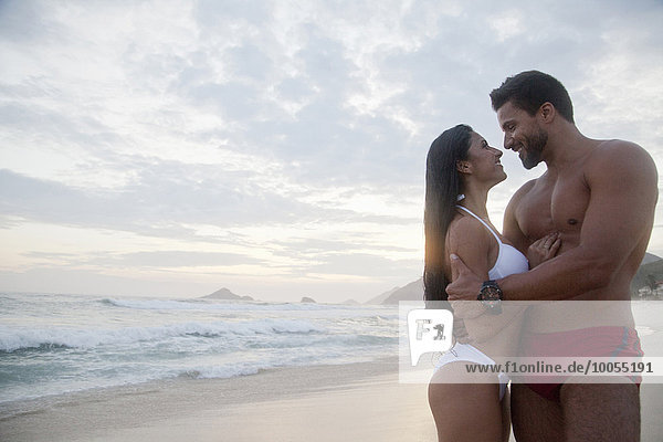 Mid adult couple standing on beach  face to face  smiling