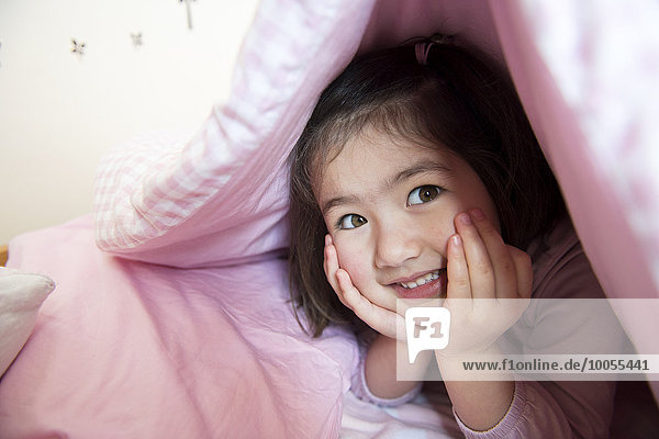 Porträt eines jungen Mädchens  versteckt unter der Bettdecke