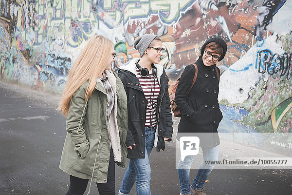 Three sisters walking by graffiti wall