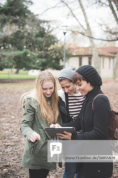 Three sisters using digital tablet in park
