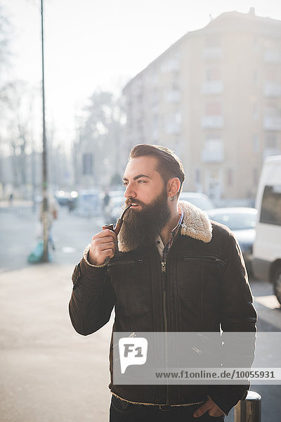 Young bearded man smoking pipe on street