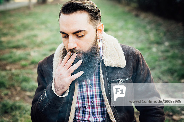 Young bearded man smoking in park