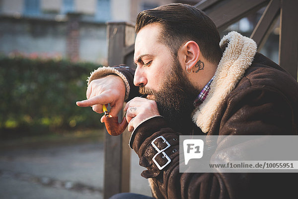 Young bearded man smoking pipe on steps