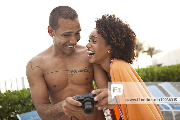 Couple laughing at photographs on digital camera at hotel poolside  Rio De Janeiro  Brazil