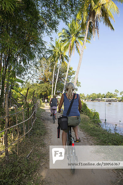 Rückansicht von zwei weiblichen Touristen  die am Mekong-Flussufer  Don Det  Laos radeln