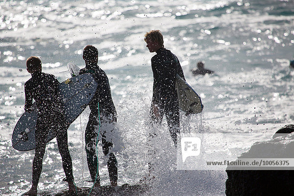 Three silhouetted male surfers standing on sea rocks  Fuerteventura  Spain