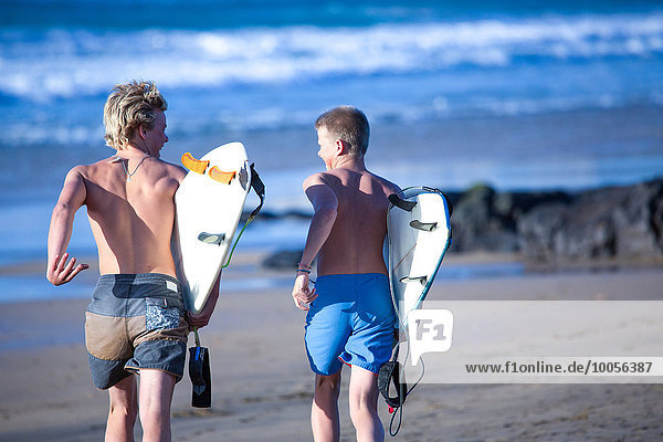 Two teenage male surfers running toward sea  Fuerteventura  Spain