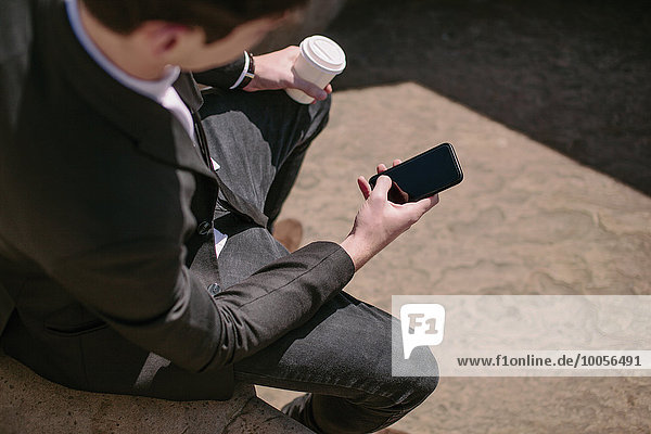 Über die Schulter des jungen Geschäftsmannes beim Lesen von Smartphone-Texten