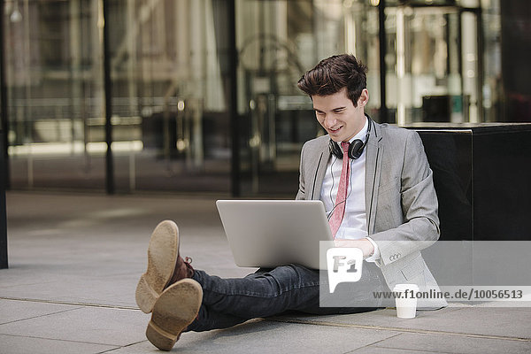 Junge Stadt Geschäftsmann sitzt auf dem Bürgersteig mit Laptop