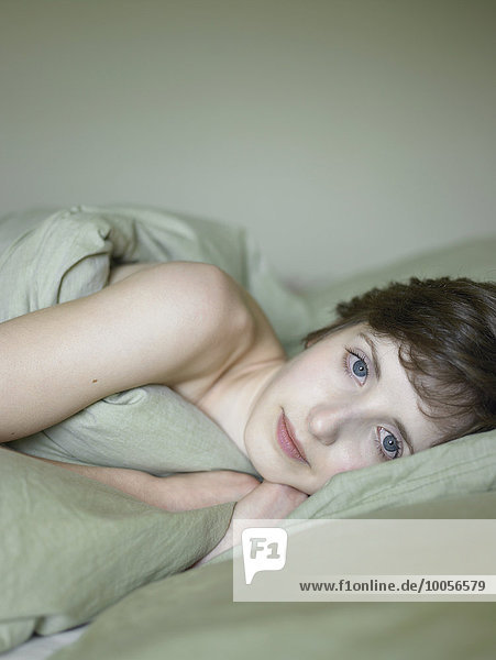 Portrait of beautiful young woman lying in bed wrapped in duvet