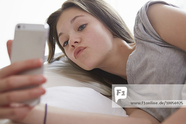 Mädchen liegt auf dem Bett und schaut auf das Smartphone.