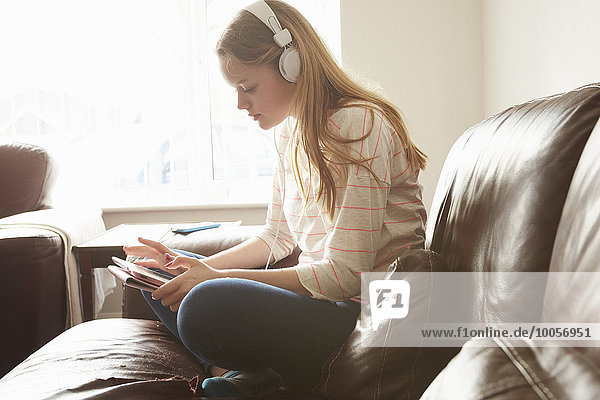 Mädchen auf dem Sofa trägt Kopfhörer und wählt Musik auf einem digitalen Tablett aus.