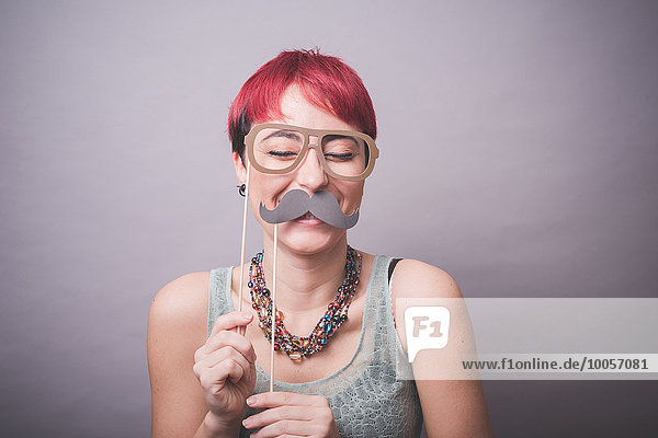 Atelierporträt einer jungen Frau mit Schnurrbart und Brille vor dem Gesicht