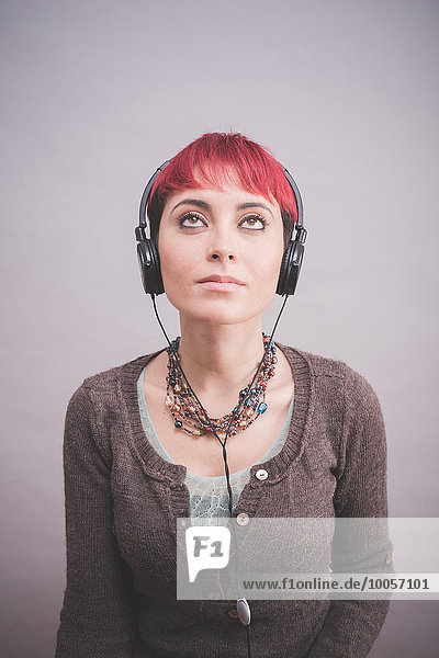 Studio-Porträt einer jungen Frau mit kurzen rosa Haaren und Kopfhörern