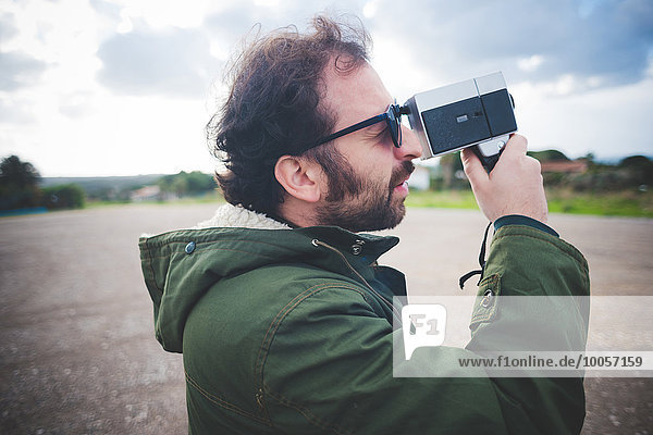 Mittlerer Erwachsener Mann mit Vintage-Filmkamera auf Brachland