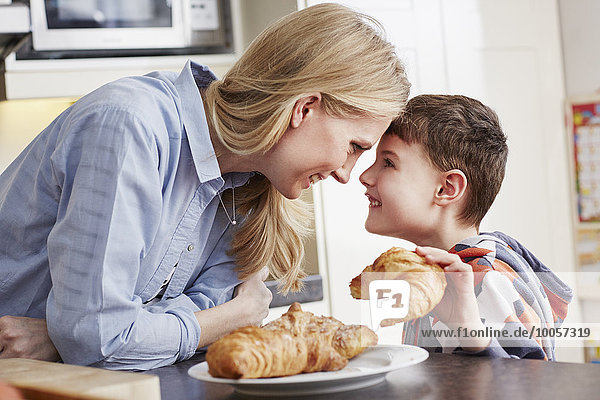 Boy holding croissant  face to face with mother