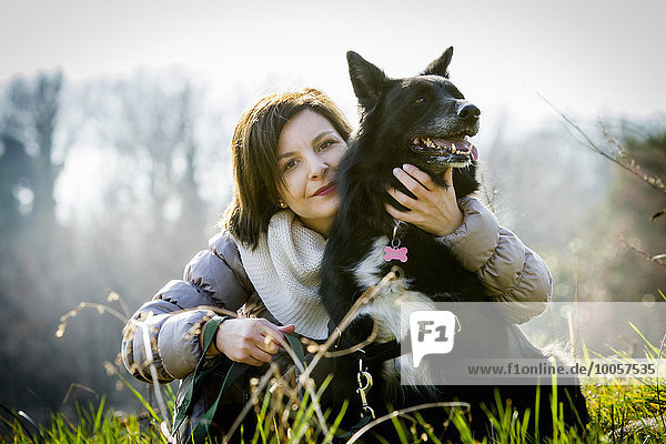 Portrait of mid adult woman with arm around her dog in field