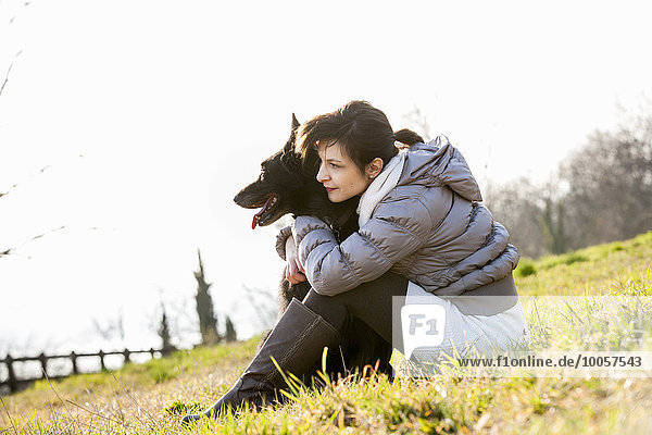 Mid adult woman and her dog sitting on hillside