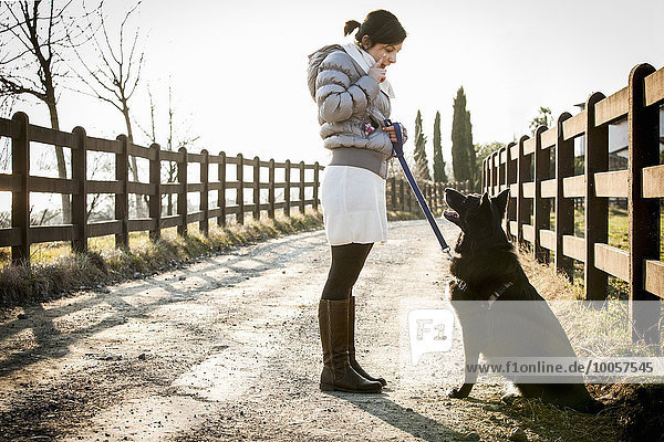 Mid adult woman training her dog to sit on rural road