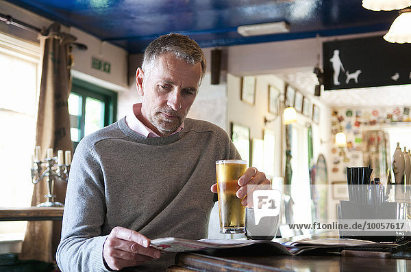 Mature man drinking beer and reading newspaper in pub