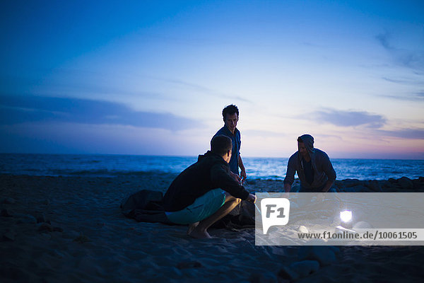 Gruppe von Freunden baut bei Sonnenuntergang ein Zelt am Strand auf.