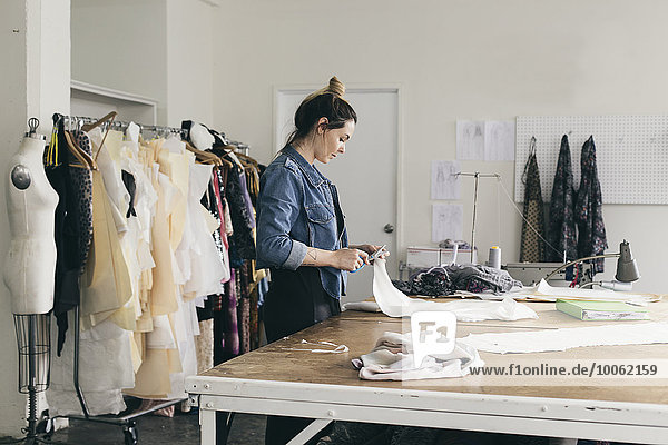 Young female seamstress cutting pattern in fashion studio