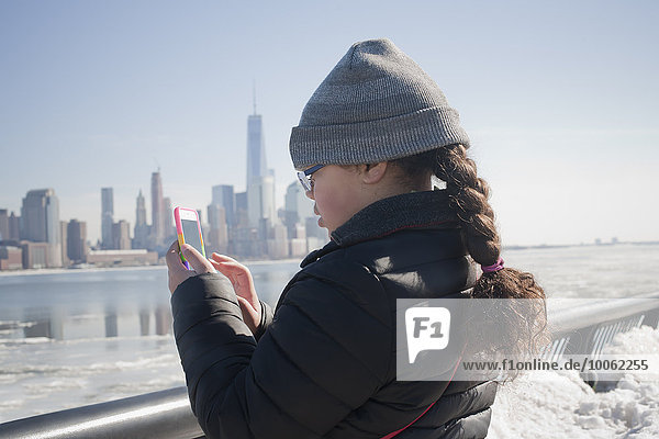 Young girl taking photograph of skyline using smartphone  New York  NY  USA