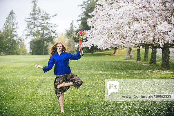 Portrait einer jungen Frau  die Yoga praktiziert  während sie einen Blumenstrauß im Park hält.