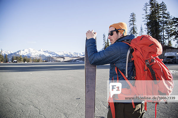 Young male skier in parking lot with distant snow capped Mount Baker  Washington  USA