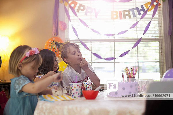 Drei Kinder sitzen am Tisch und essen lila Geburtstagskuchen.