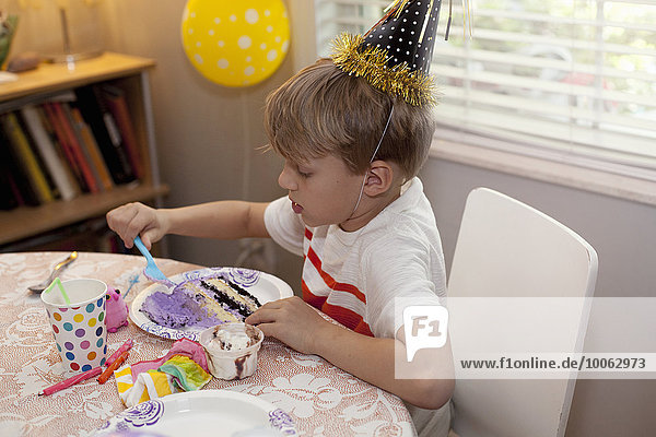 Boy in party hat sitting at table eating birthday cake