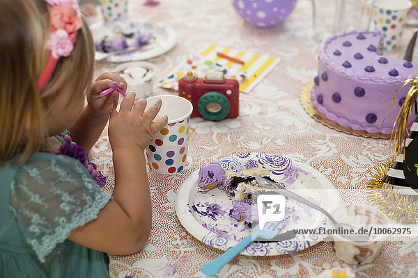 Seitenansicht des Mädchens  das am Geburtstagstisch sitzt und lila Kuchen isst.