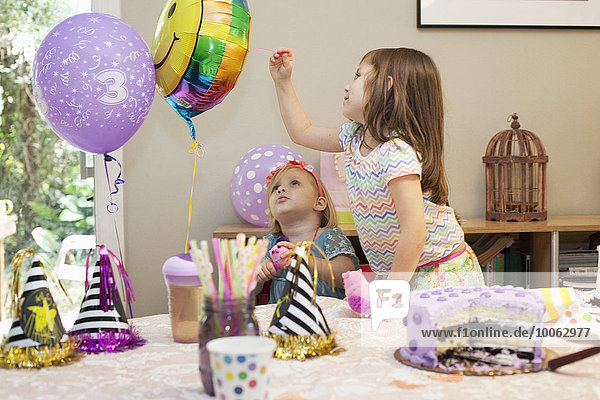 Zwei Mädchen sitzen am Geburtstagstisch und spielen mit Luftballons.
