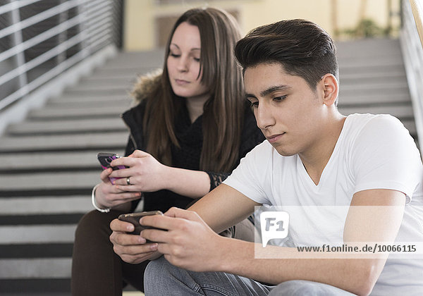 Zwei Jugendliche sitzen auf einer Treppe und schauen in ihr Smartphone