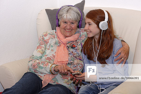Granddaughter and grandmother listening to music through headphones  digital music  Bavaria  Germany  Europe