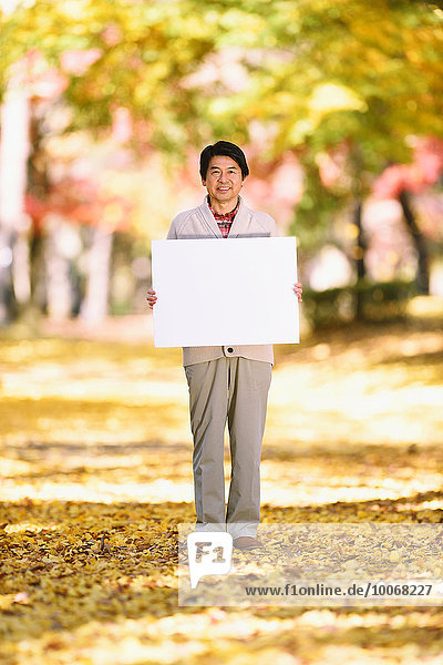 Senior Japanese man with whiteboard in a city park in Autumn