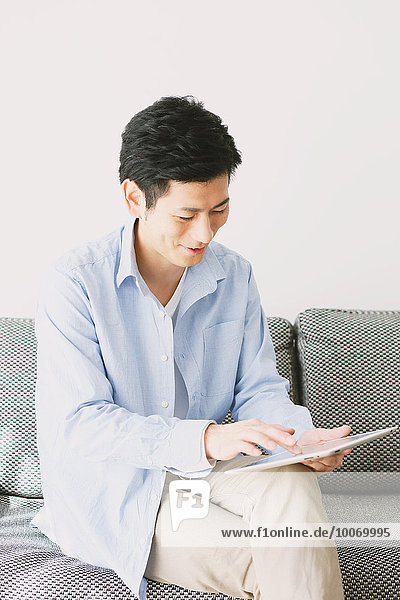 Young Japanese man with tablet on the sofa