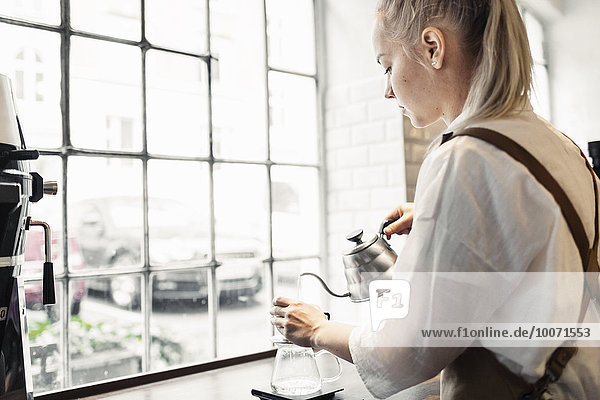 Seitenansicht der weiblichen Barista bei der Kaffeezubereitung am Café-Tresen am Fenster