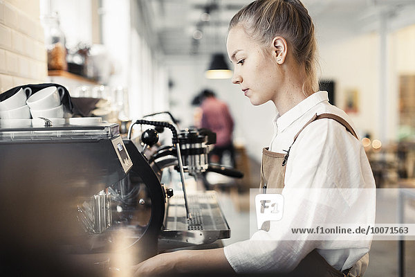 Side view of young female barista using espresso maker at cafe