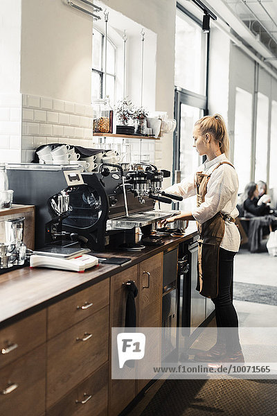 Volle Länge der weiblichen Barista mit Kaffeemaschine im Cafe