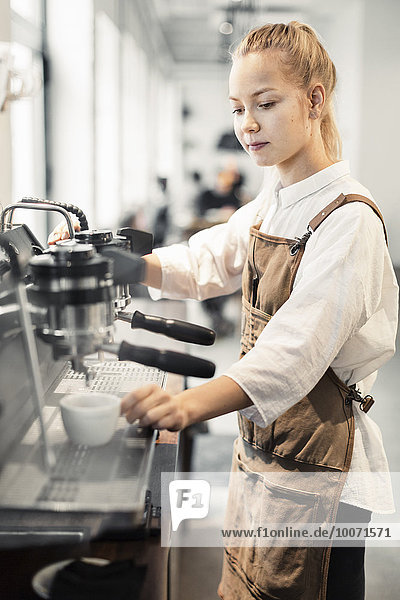 Young female barista using coffee maker at cafe